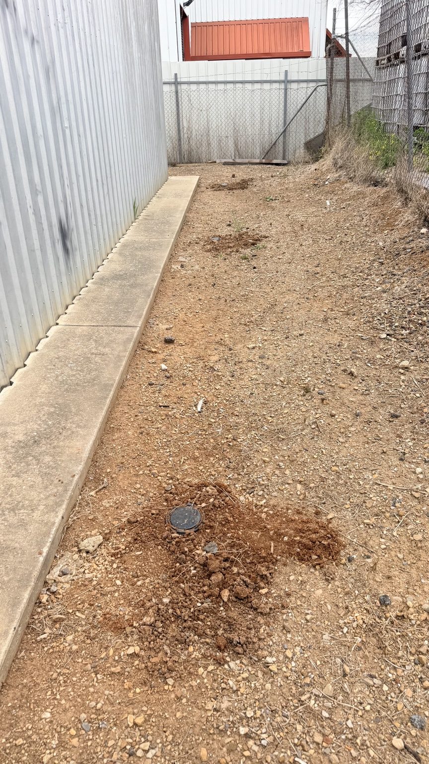 Termite station installed in soil beside a commercial warehouse